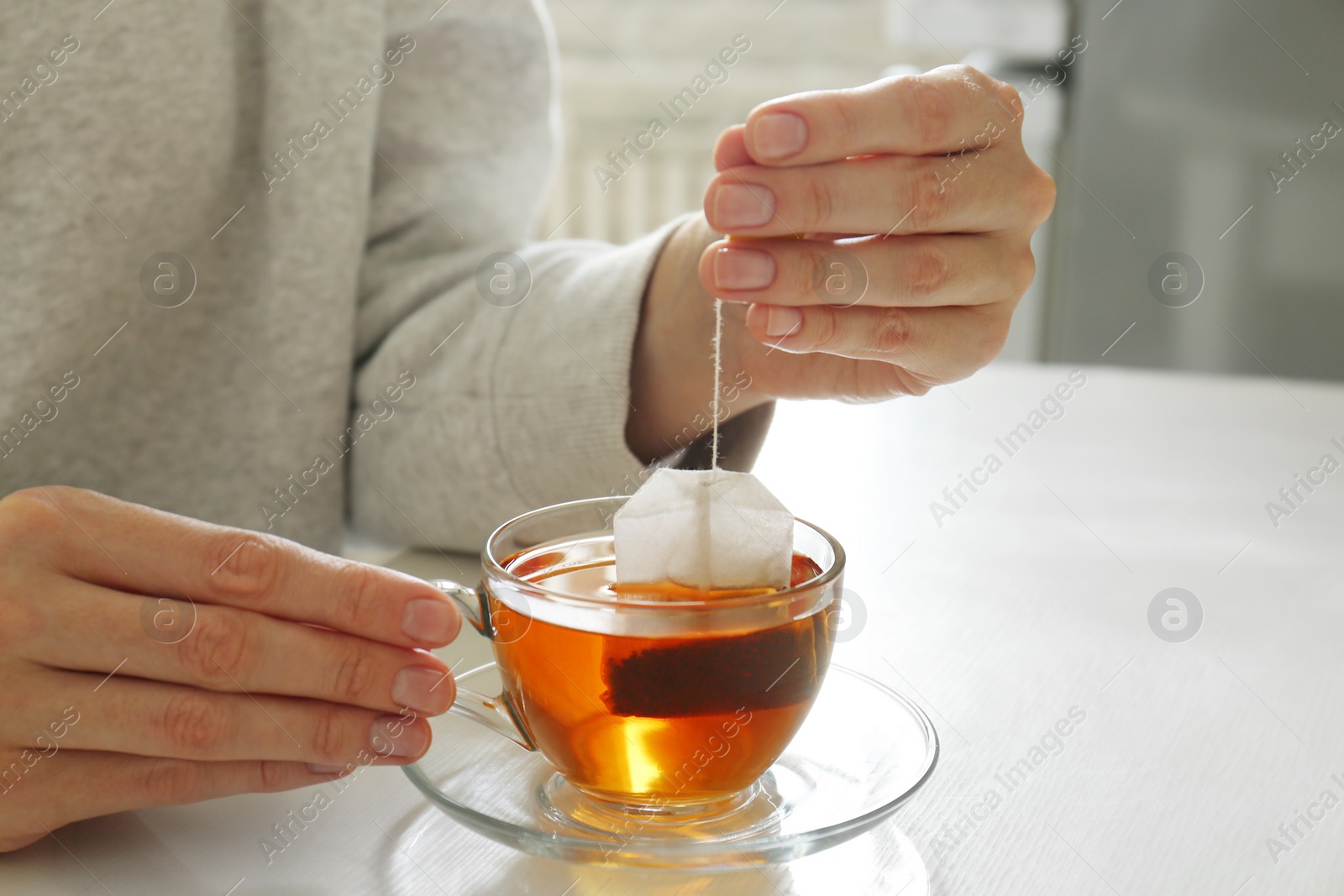 Photo of Woman taking tea bag out of cup at table indoors, closeup