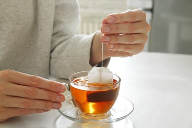 Photo of Woman taking tea bag outcup at table indoors, closeup