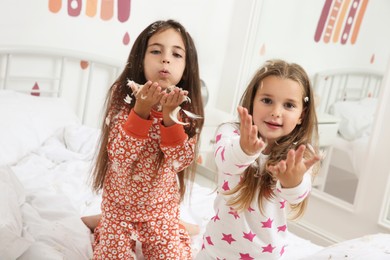 Photo of Cute little girls in pajamas playing with feathers on bed at home. Happy childhood