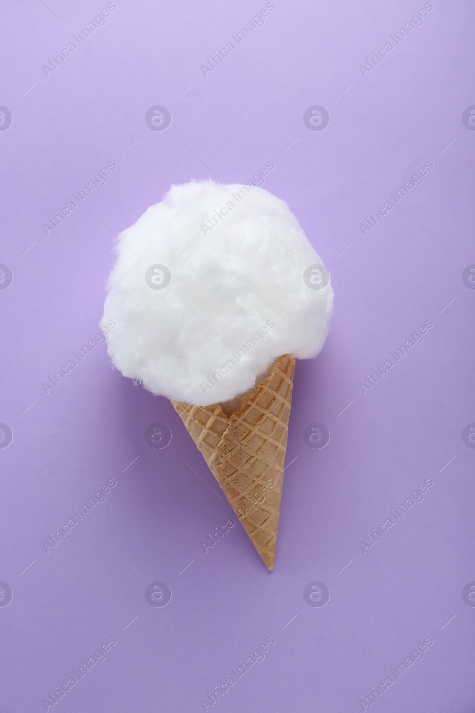 Photo of Sweet cotton candy in waffle cone on purple background, top view