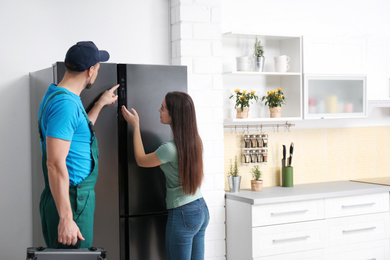 Male technician talking with client near refrigerator in kitchen