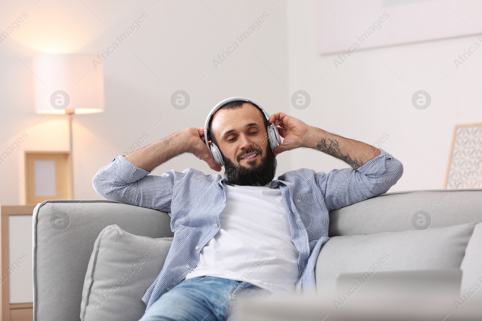 Photo of Mature man with headphones resting on sofa at home