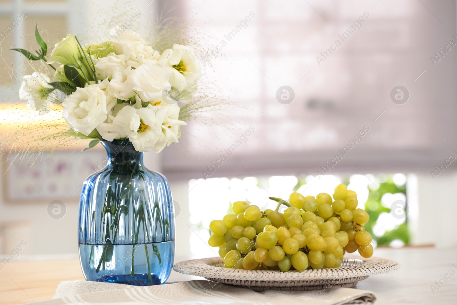 Photo of Bouquet of beautiful eustoma flowers and grapes on white table in kitchen. Interior design