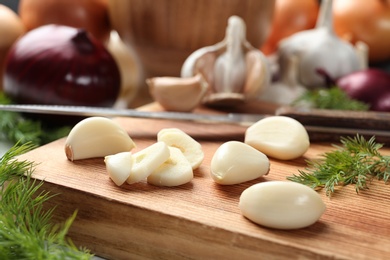 Photo of Wooden board with garlic cloves on table, closeup