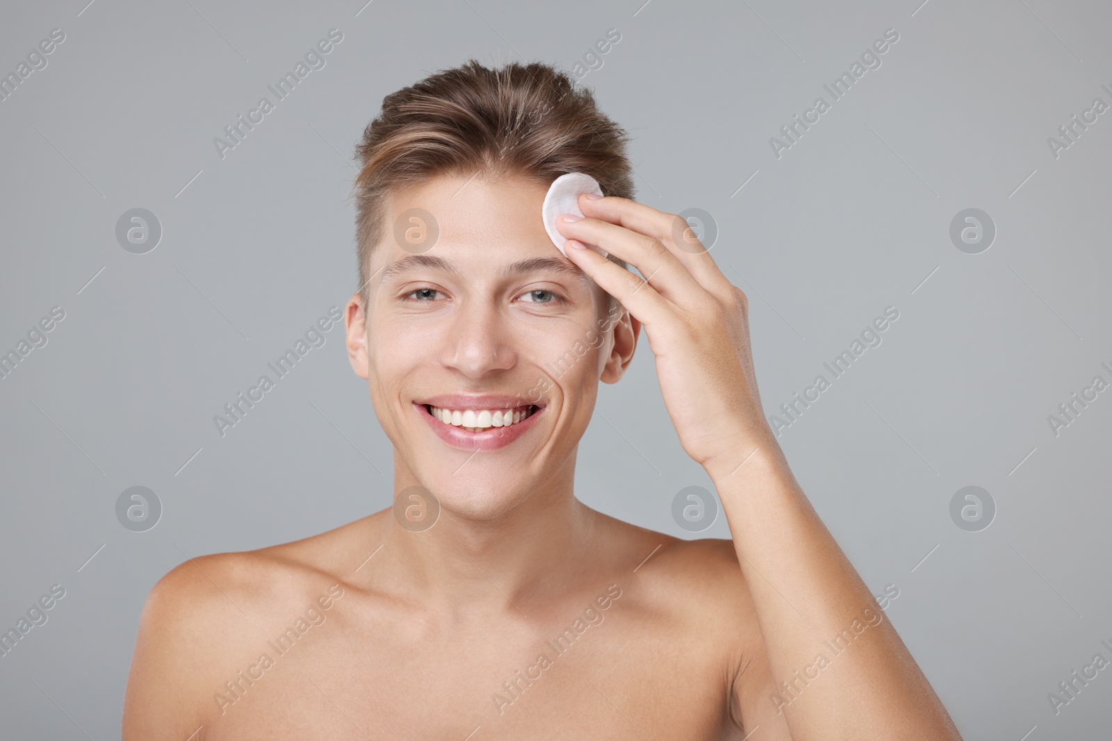 Photo of Handsome man cleaning face with cotton pad on grey background