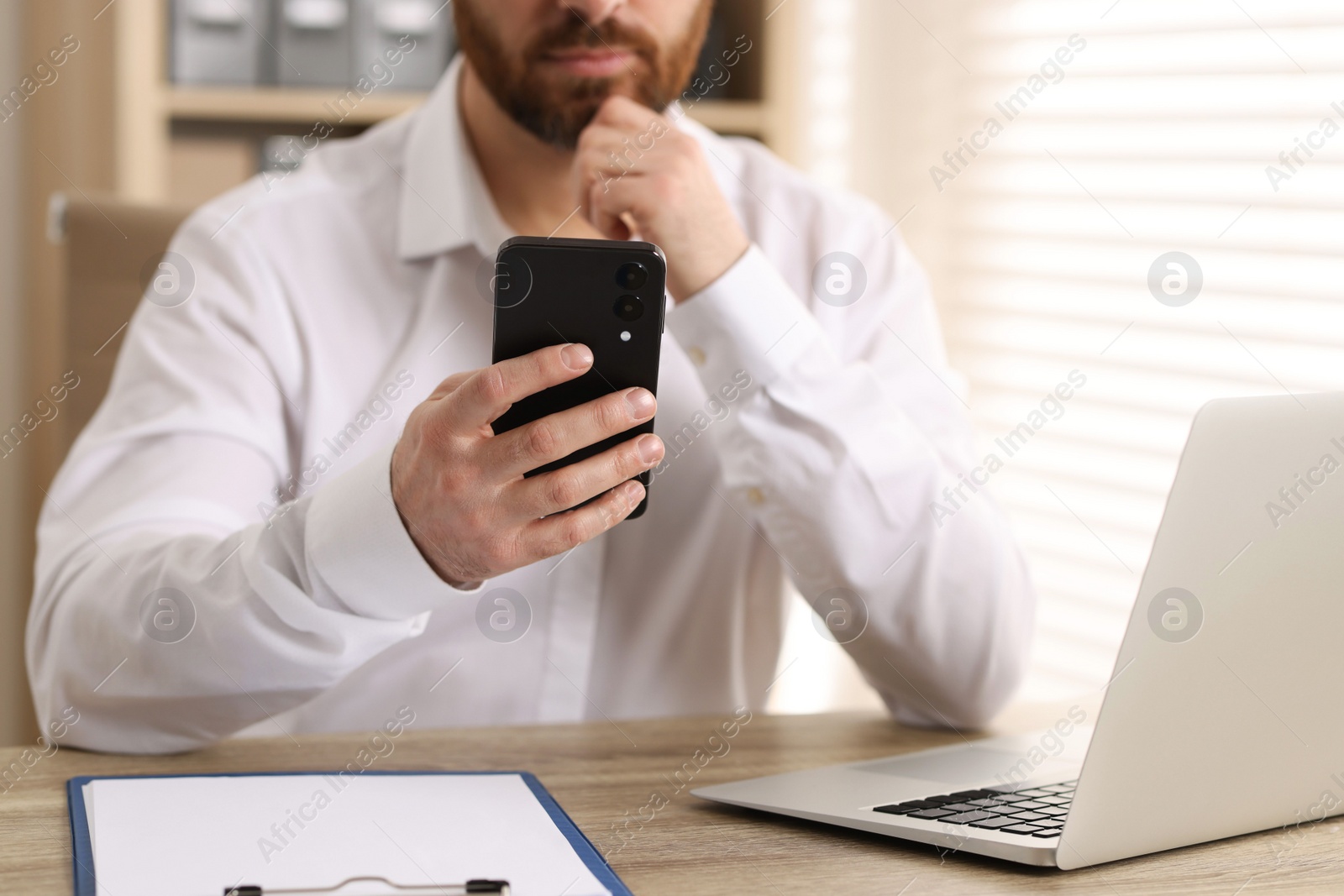 Photo of Man using smartphone at table in office, closeup