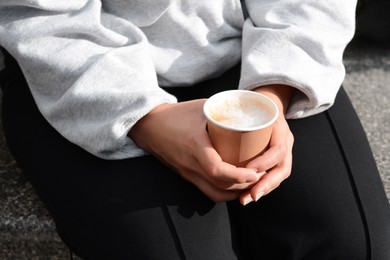 Photo of Woman sitting with cardboard cup of coffee, closeup