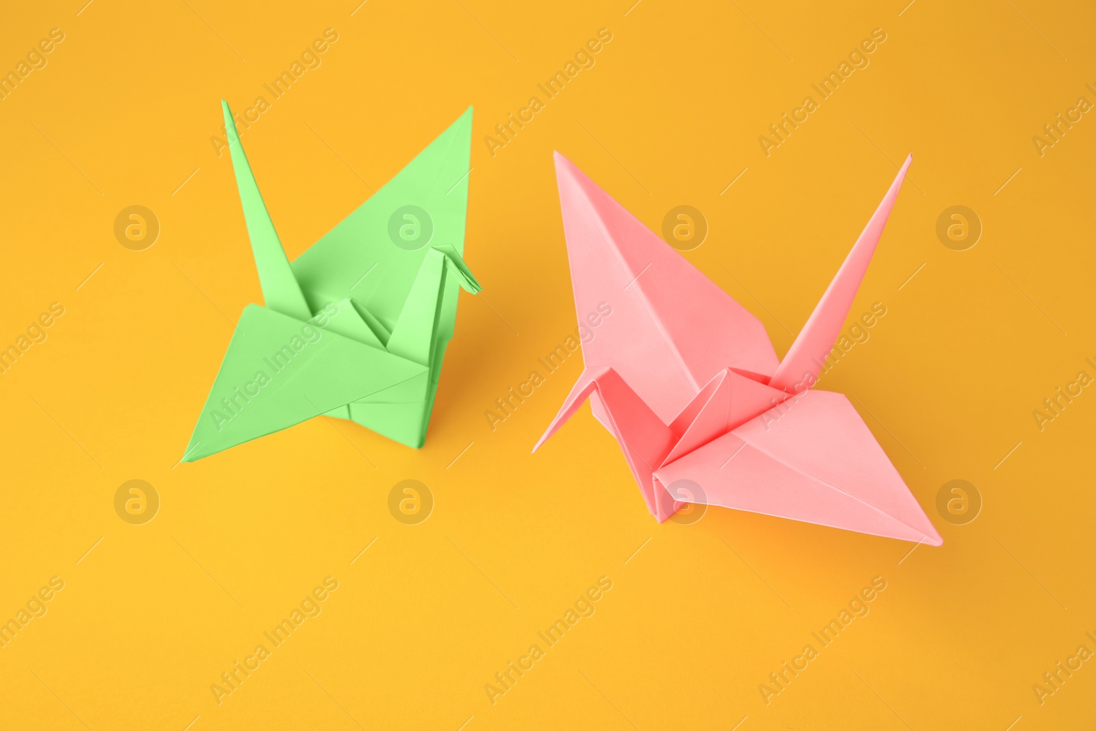 Photo of Origami art. Beautiful light green and pale pink paper cranes on orange background