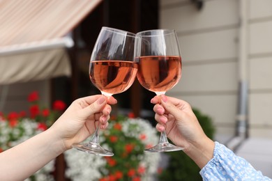 Photo of Women clinking glasses with rose wine outdoors, closeup