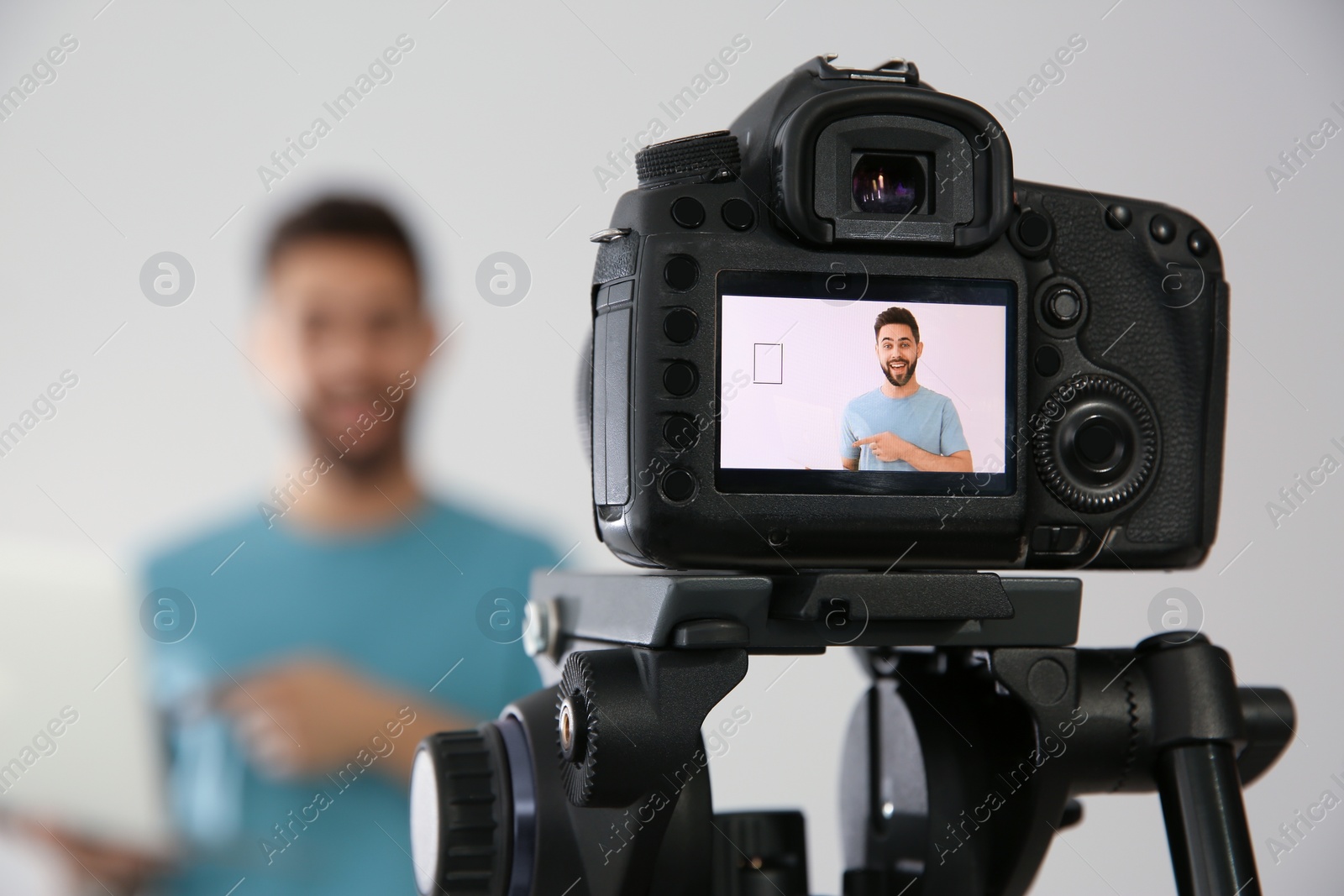 Photo of Young blogger with laptop shooting video with camera against white background, focus on screen