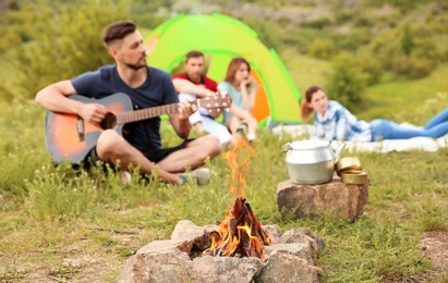 Photo of Group of people resting outdoors, focus on bonfire. Camping season