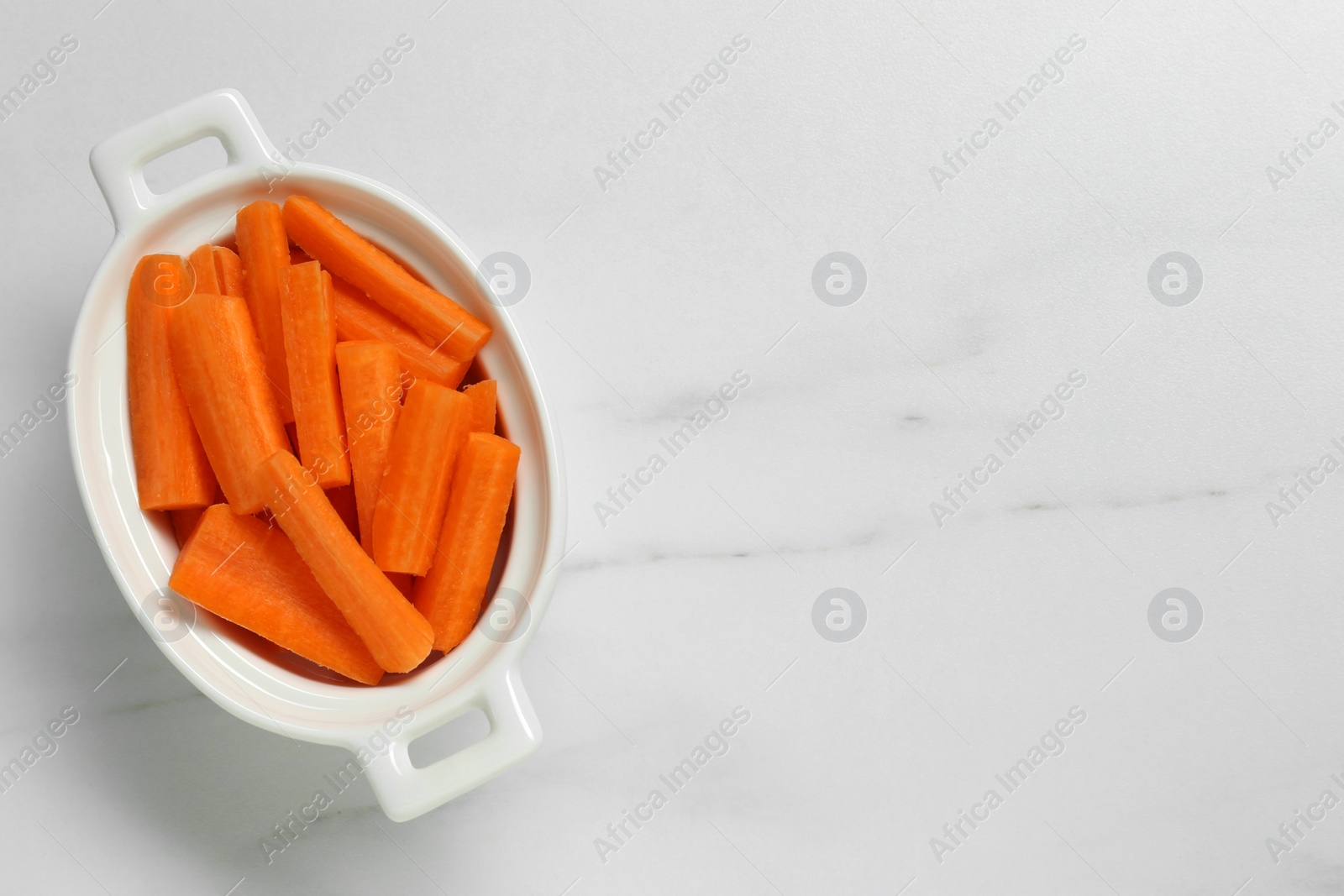 Photo of Cut carrots in bowl as finger food on white marble table, top view. Space for text