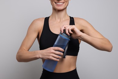 Sportswoman with bottle of water on light grey background, closeup