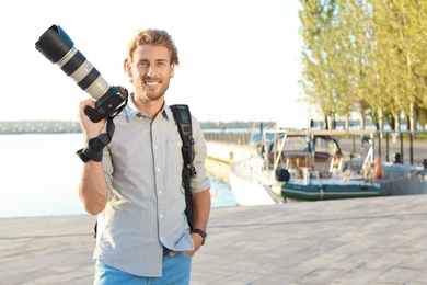 Photo of Young male photographer holding professional camera at pier. Space for text