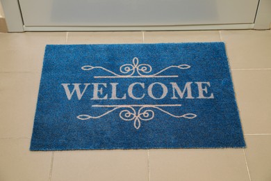 Photo of Beautiful blue doormat with word Welcome on floor near entrance