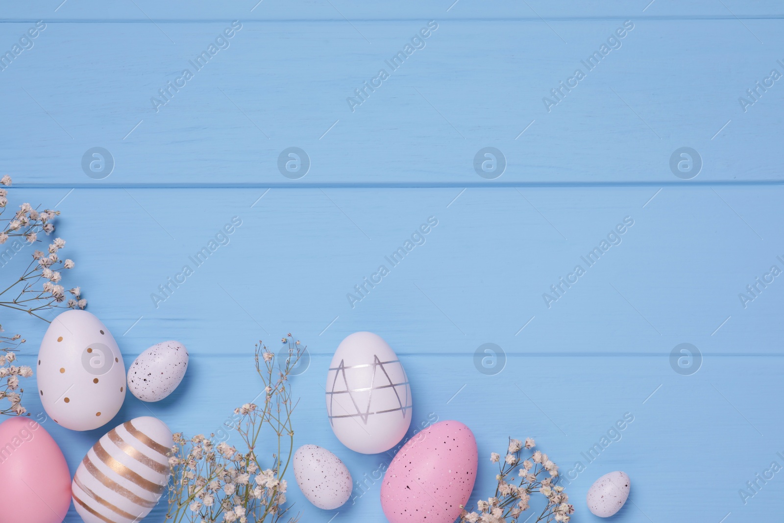 Photo of Flat lay composition with festively decorated Easter eggs and gypsophila flowers on light blue wooden table. Space for text