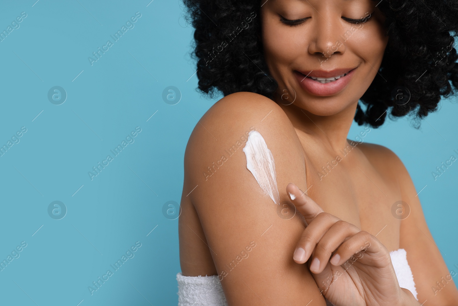 Photo of Young woman applying body cream onto shoulder on light blue background, closeup. Space for text