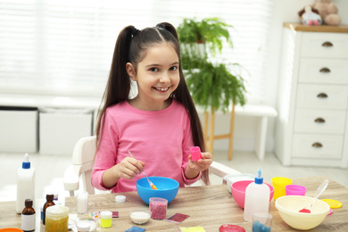 Photo of Cute little girl mixing ingredients with silicone spatula at table. DIY slime toy