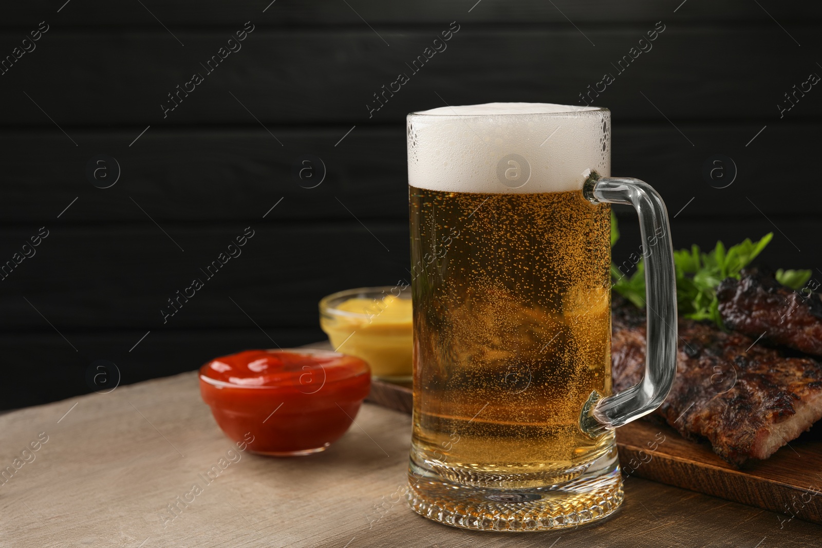 Photo of Mug with beer, delicious grilled ribs and sauces on wooden table. Space for text