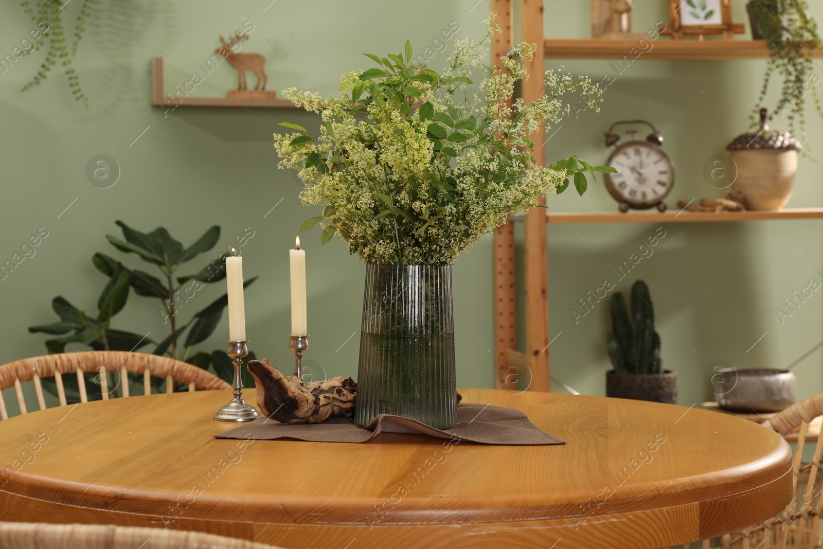 Photo of Vase with beautiful flowers and candles on wooden table in stylish dining room