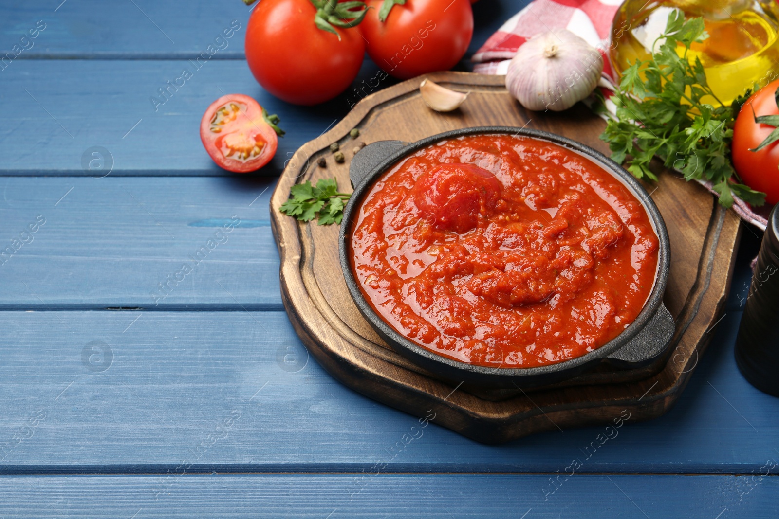 Photo of Homemade tomato sauce in bowl and fresh ingredients on blue wooden table, space for text