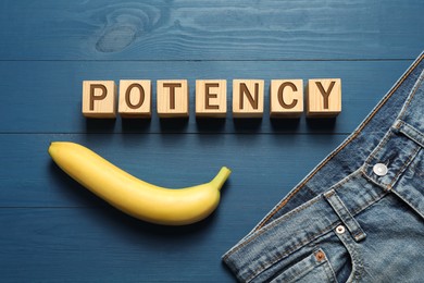 Photo of Men jeans, banana and cubes with word Potency on blue wooden table, flat lay