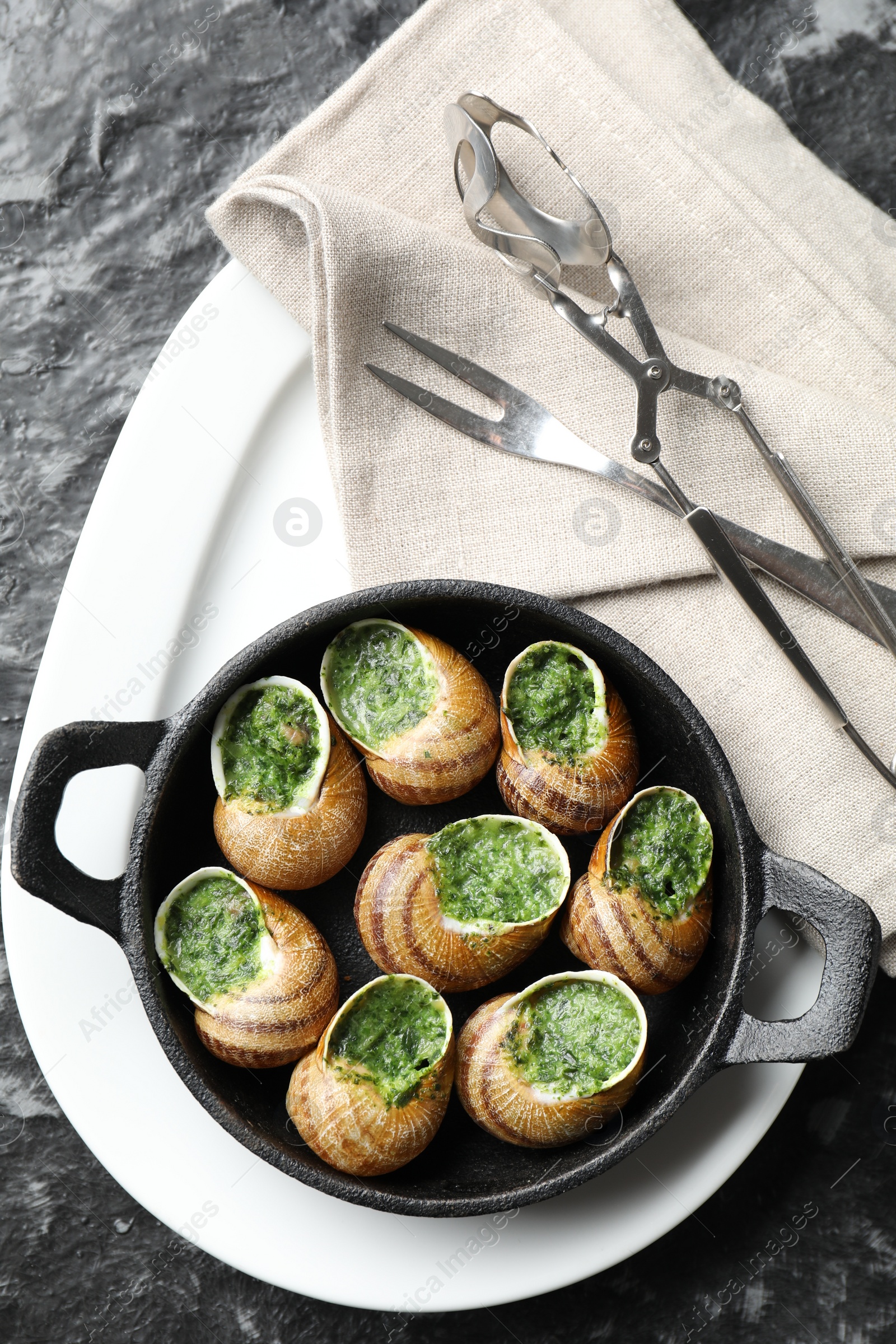 Photo of Delicious cooked snails in baking dish served on grey textured table, flat lay