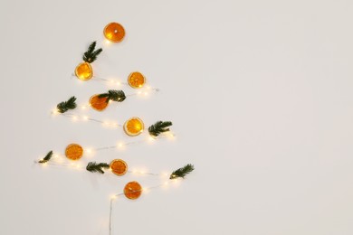 Christmas decor made of dry orange slices, festive lights and fir tree branches on white wall. Space for text