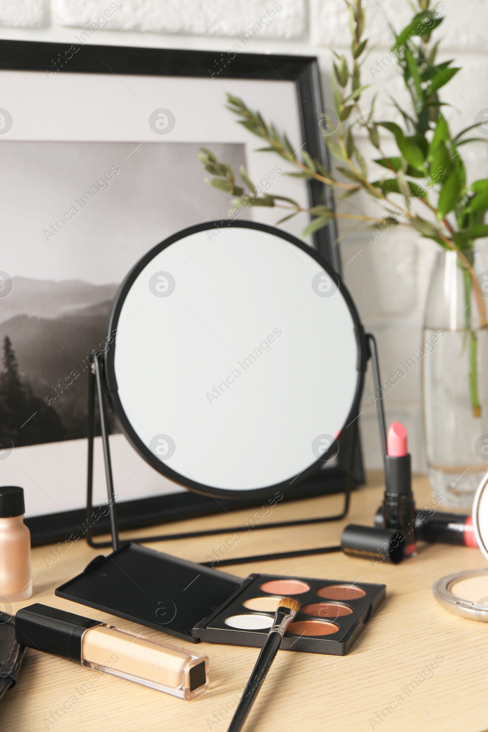 Photo of Mirror and makeup products on wooden dressing table, closeup