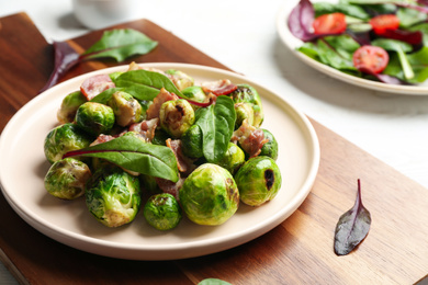 Photo of Delicious Brussels sprouts with bacon on wooden board, closeup