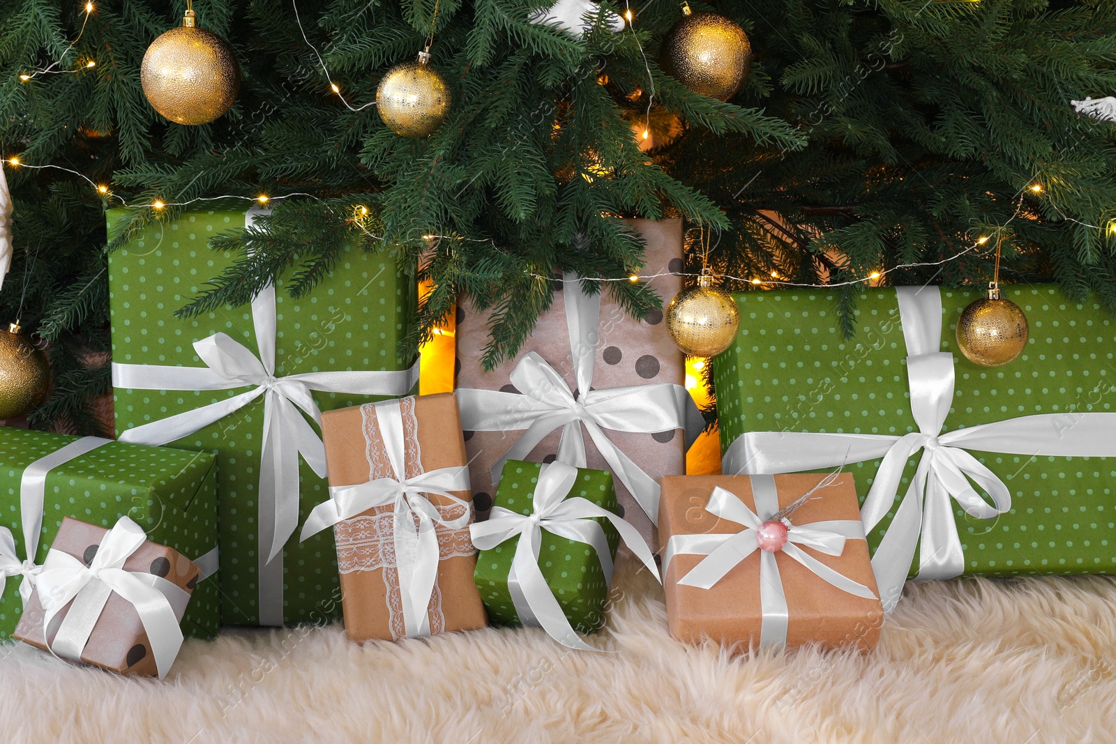 Photo of Many gift boxes under Christmas tree decorated with ornaments and festive lights in room