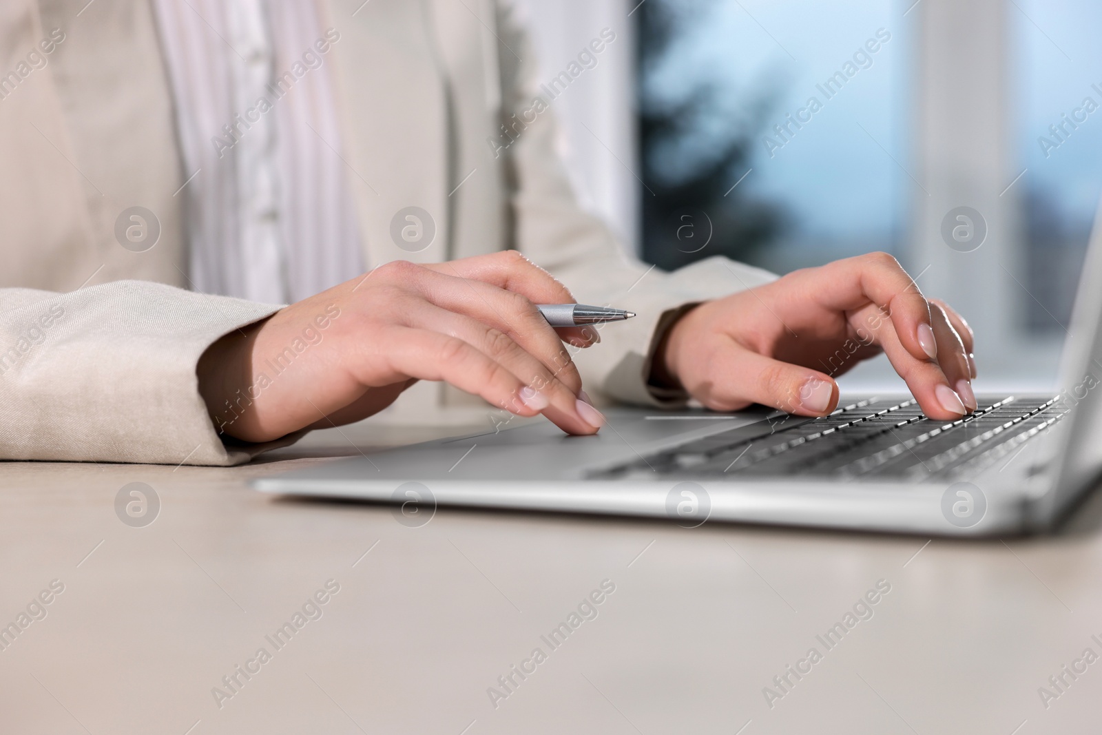 Photo of Woman with pen working on laptop at wooden table, closeup. Electronic document management