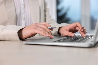 Photo of Woman with pen working on laptop at wooden table, closeup. Electronic document management