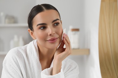 Photo of Beautiful woman removing makeup with cotton pad indoors