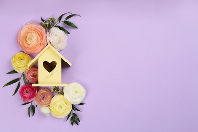 Stylish bird house and fresh flowers on violet background, flat lay. Space for text