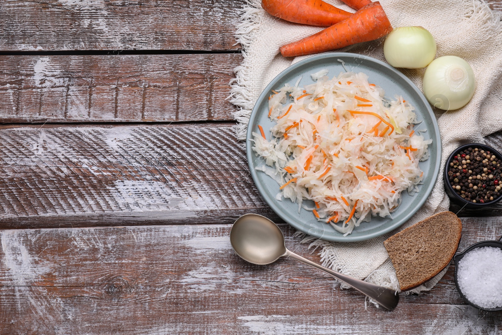 Photo of Bowl of tasty sauerkraut and ingredients on wooden table, flat lay. Space for text