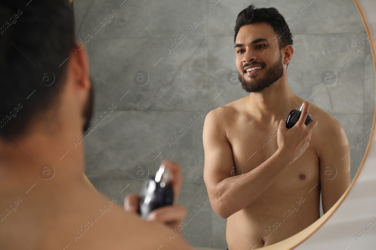 Photo of Man spraying luxury perfume near mirror indoors