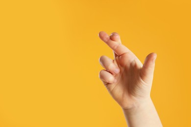Child holding fingers crossed on yellow background, closeup with space for text. Good luck superstition