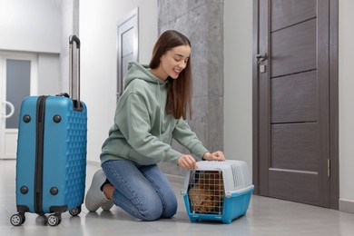 Photo of Travelling with pet. Smiling woman looking at carrier with her dog in hall