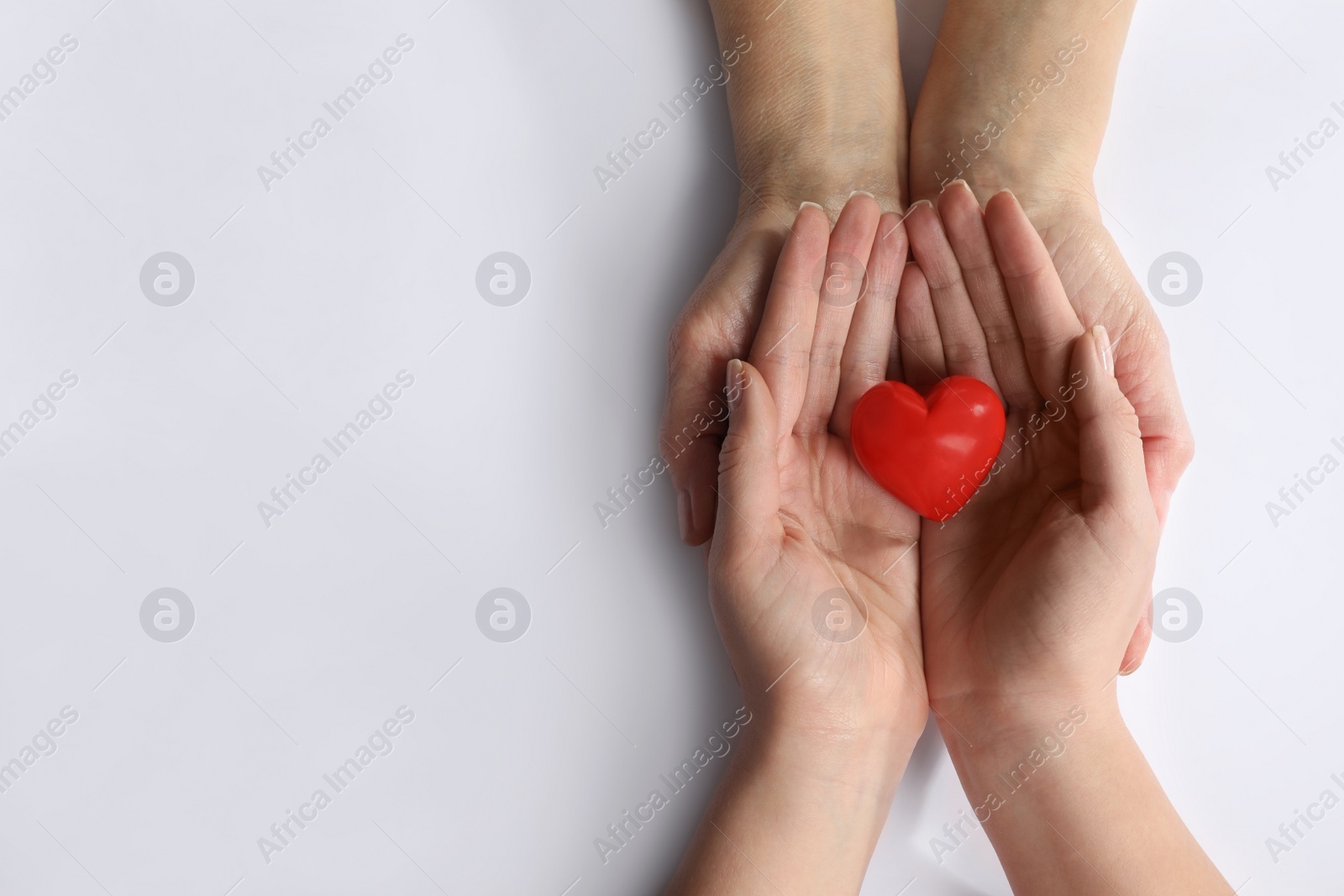 Photo of Young and elderly women holding red heart on white background, top view