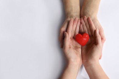 Young and elderly women holding red heart on white background, top view