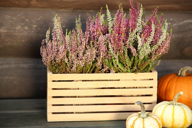 Photo of Beautiful heather flowers in crate and pumpkins on table near wooden wall