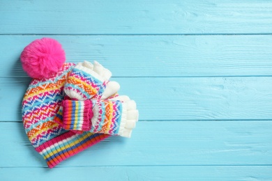 Photo of Warm knitted hat and mittens on blue wooden background, flat lay. Space for text