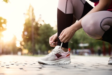 Woman tying shoelaces before morning run in park, closeup. Space for text