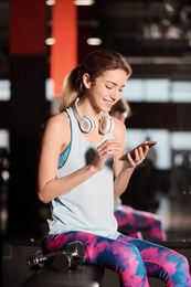 Photo of Young woman with headphones and mobile device at gym