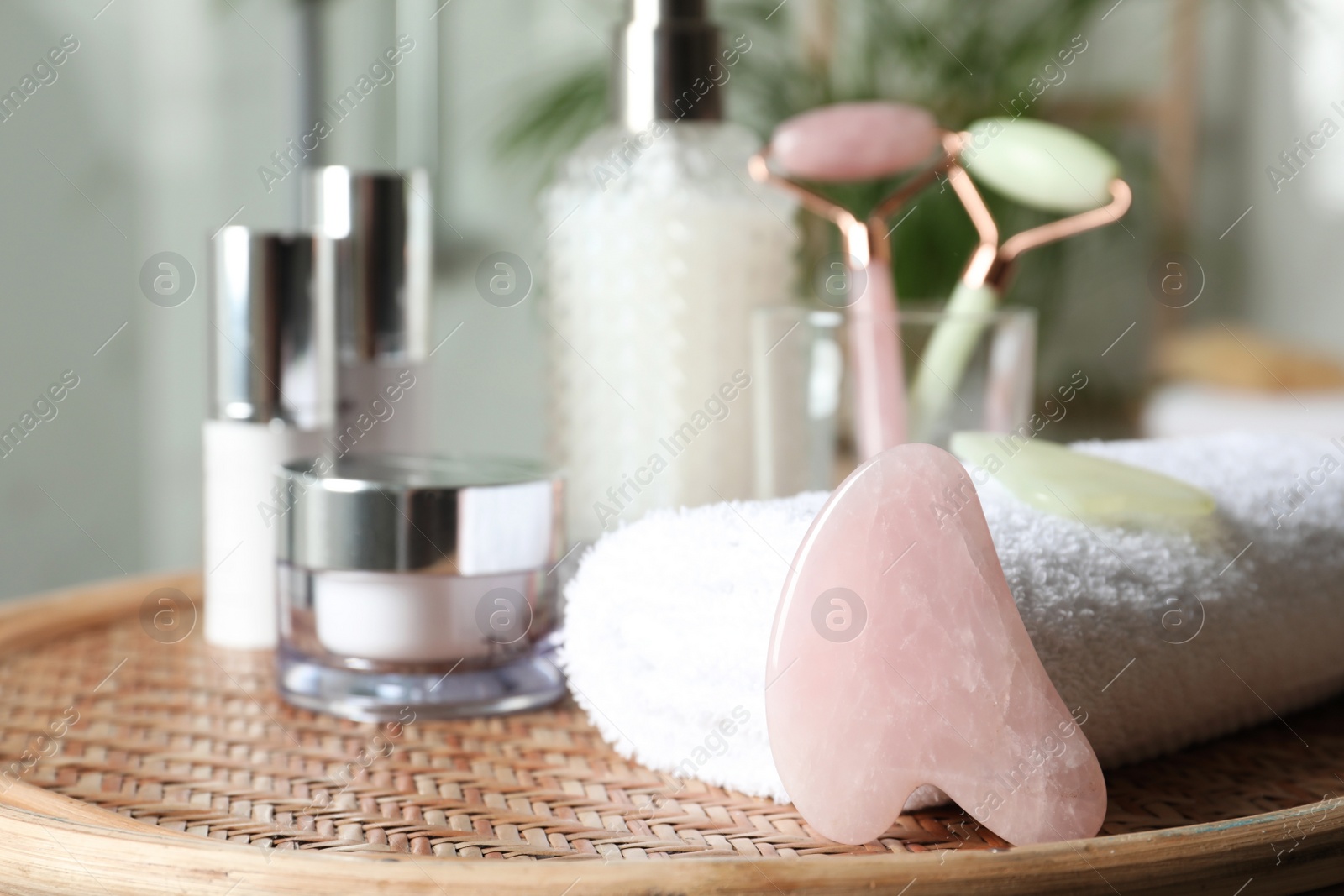 Photo of Rose quartz gua sha tool, natural face rollers and toiletries on wicker table indoors. Space for text