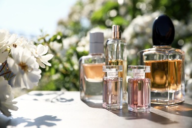 Photo of Bottles with luxury perfumes on table in garden, space for text