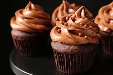 Photo of Delicious chocolate cupcakes with cream and beads on black table, closeup