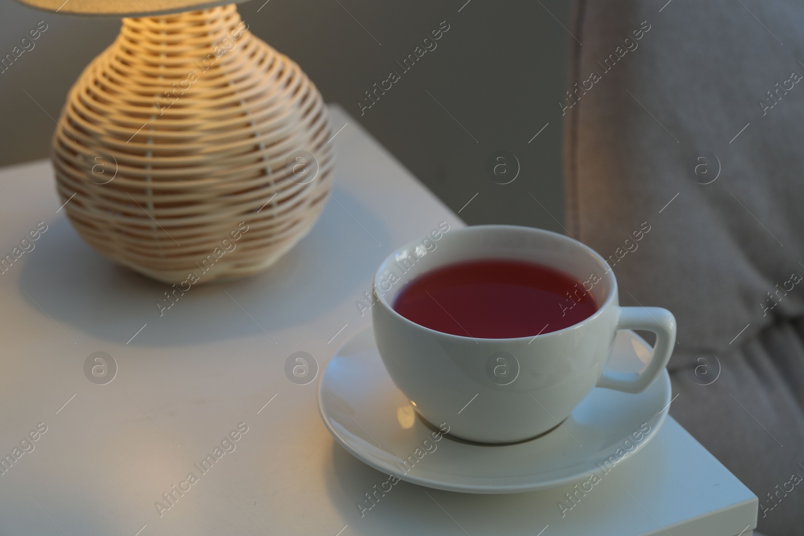 Photo of Cup of hot tea and nightlight on white table at night