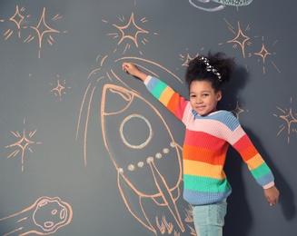 Photo of African-American child playing with chalk rocket drawing on grey background